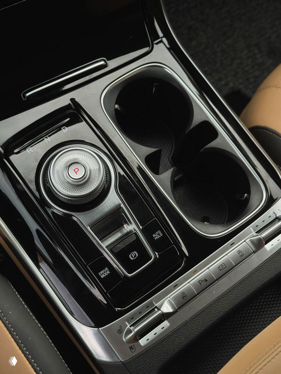Селектор коробки передач в виде вращающейся шайбы и два подстаканника в центральной консоли KIA Carnival, глянцевая чёрная отделка.