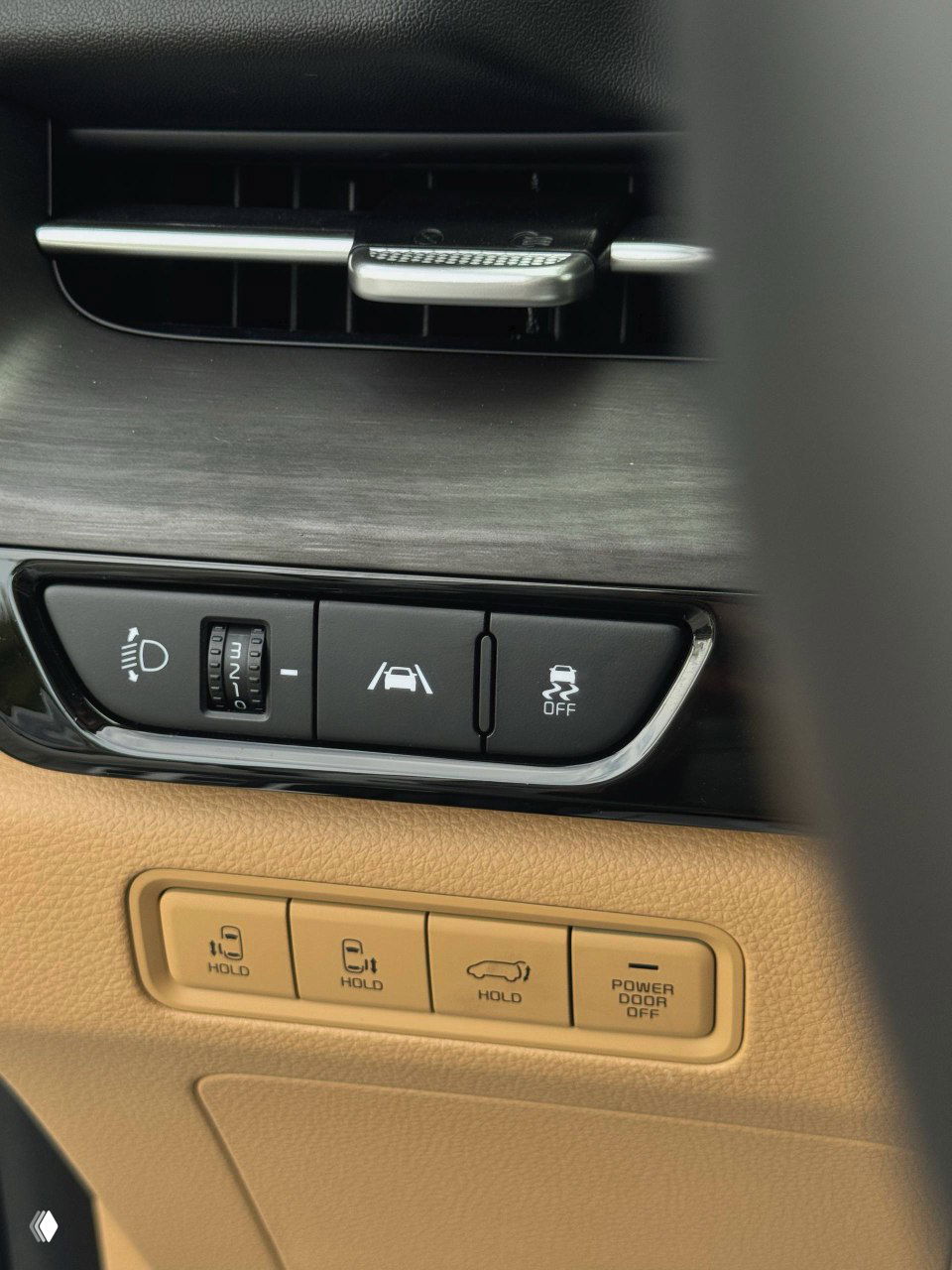 Блок управления ассистентами на дверной панели и воздуховод в интерьере KIA Carnival, контрастная отделка чёрного и бежевого цвета.