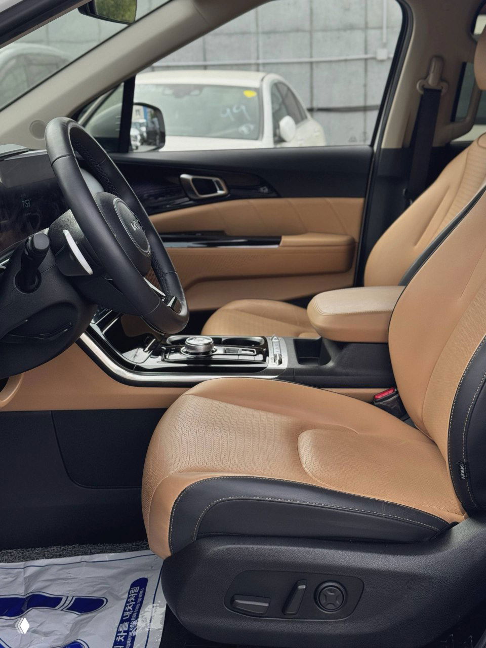 Переднее пассажирское сиденье и панорамный вид на часть передней консоли, бежевые кожаные сиденья KIA Carnival и отделка дверей.