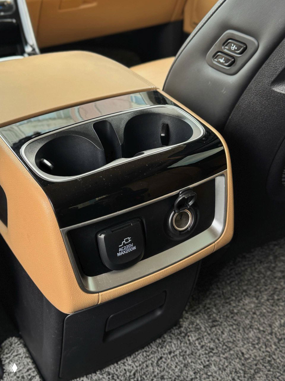 Центральная консоль между задними сиденьями с двумя подстаканниками и розеткой 220V в салоне KIA Carnival, отделка бежевым пластиком.