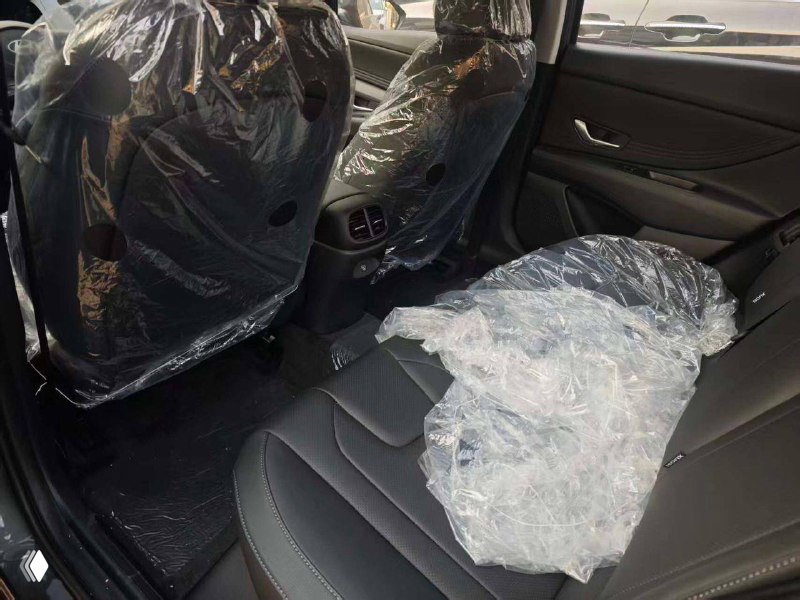 Задние сиденья Hyundai Elantra в автосалоне: чёрная обивка и защитная плёнка, вид на пространство для пассажиров и коврики.