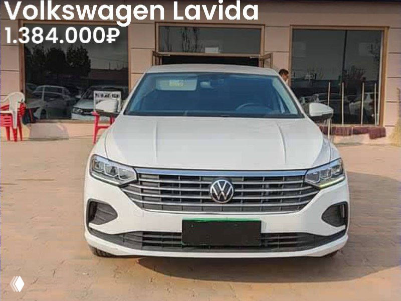 Белый Volkswagen Lavida с фронтальным ракурсом на стоянке; на фото видно модель и цену 1.384.000₽, окружение автосалона.
