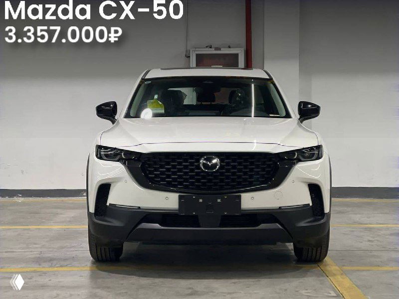 Фронтальный вид белой Mazda CX-50 на парковке склада, крупный план решетки радиатора и цена 3.357.000₽, современный интерьер стоянки.