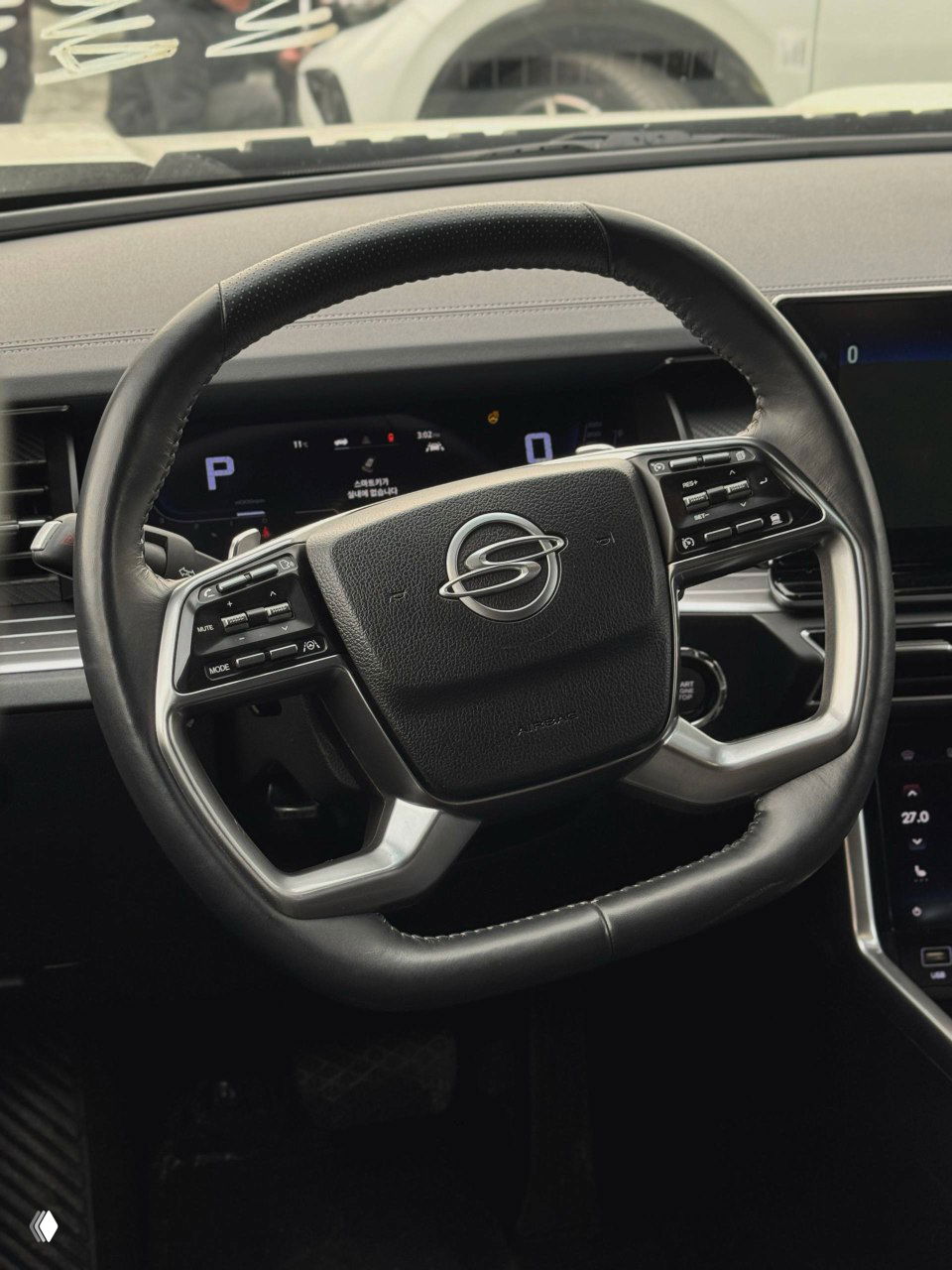 Рулевое колесо с логотипом SsangYong и элементы управления: вид на руль и цифровую приборную панель автомобиля.