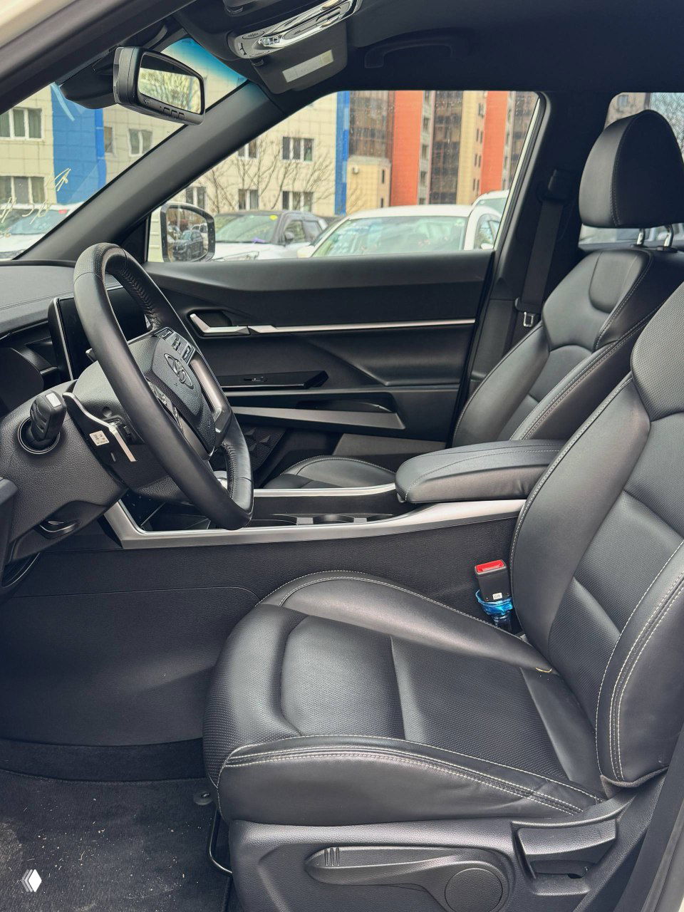 Передние кресла и панорамный вид салона SsangYong Torres: чёрная кожаная обивка, подлокотник и элементы декора.