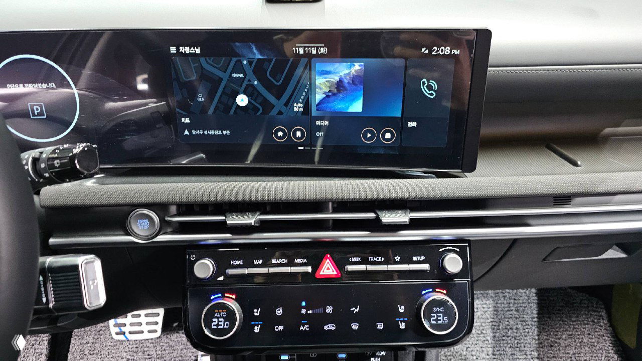 Широкий дисплей мультимедиа и панель управления Hyundai Tucson 2025 с отображением навигации и медиа, крупный план экранов и органов управления климатом.