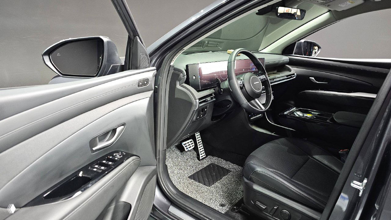 Водительская дверь и переднее сиденье Hyundai Tucson 2025: вид с открытой дверью, элементы управления окнами и отделка дверной карты, салон в серой гамме.