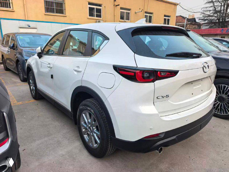 Задняя часть белой Mazda CX-5 2025 на стоянке: видны задние фары, бампер, надпись CX-5 и общая геометрия кузова с правого ракурса.