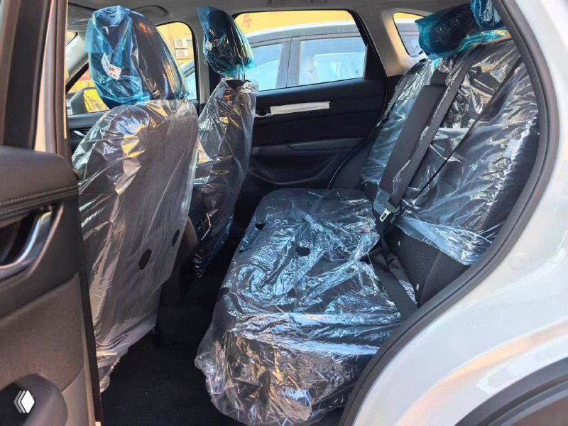 Задние пассажирские сиденья Mazda CX-5 2025 с защитной плёнкой: видно пространство для ног, три посадочных места и отделку салона в задней части.