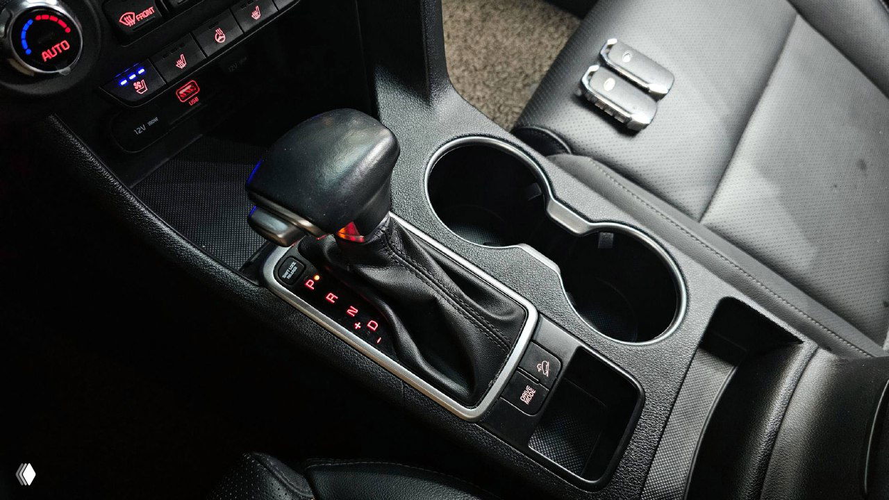 Ближний план центральной консоли KIA Sportage: селектор АКПП, подстаканники и элементы управления, состояние кожаной обивки.