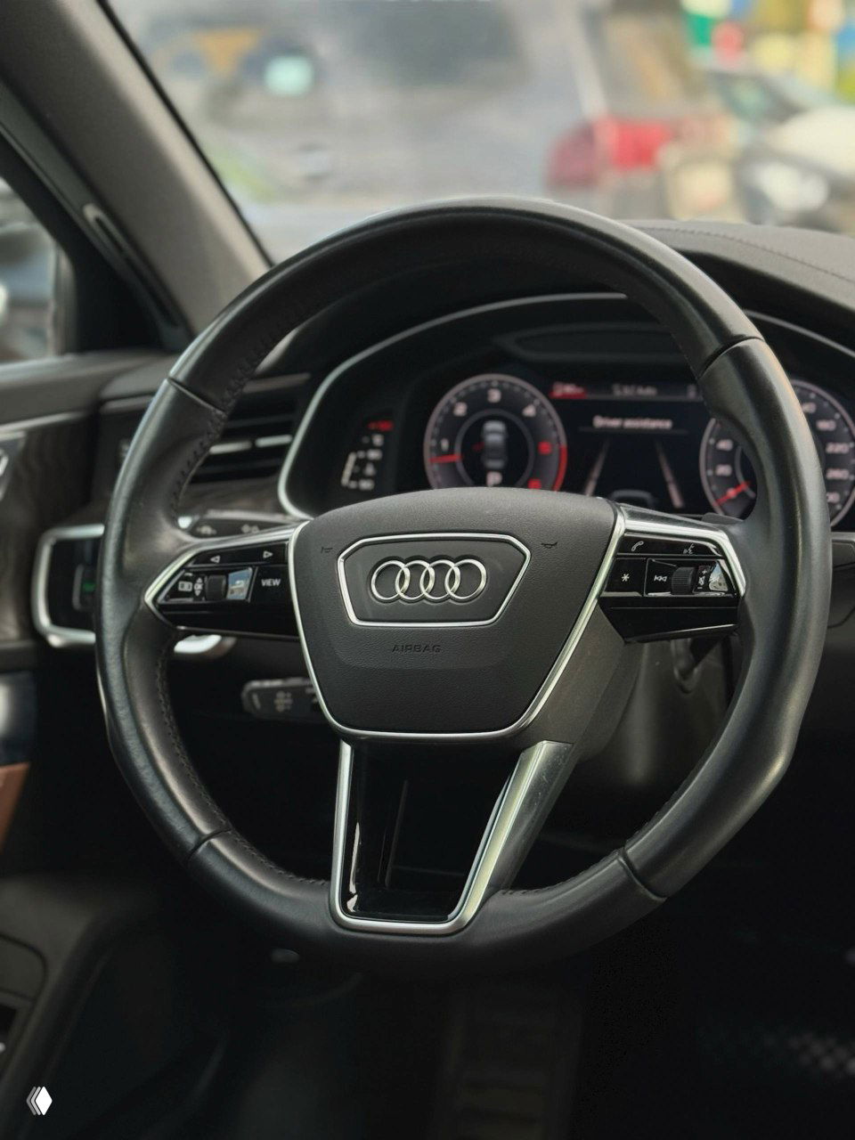 Рулевое колесо Audi с логотипом кольца Audi, вид на виртуальную панель приборов и элементы управления на руле.