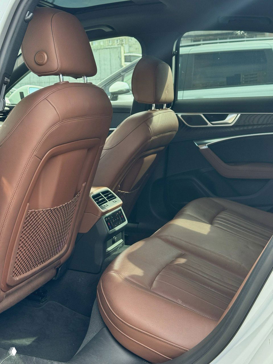 Задний ряд сидений Audi A6 с коричневой кожаной обивкой, вид на систему климат-контроля и просторнось салона.