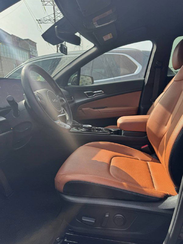 Вид на переднее пассажирское сиденье и водительскую зону KIA Sportage: коричневый салон, контурные сиденья и общий вид интерьера при дневном свете.