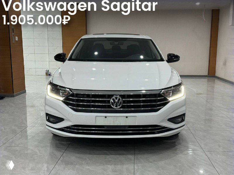 Фронтальный вид белого Volkswagen Sagitar 2021 года в зале, видна решётка и цена 1.905.000₽, аккуратное освещение