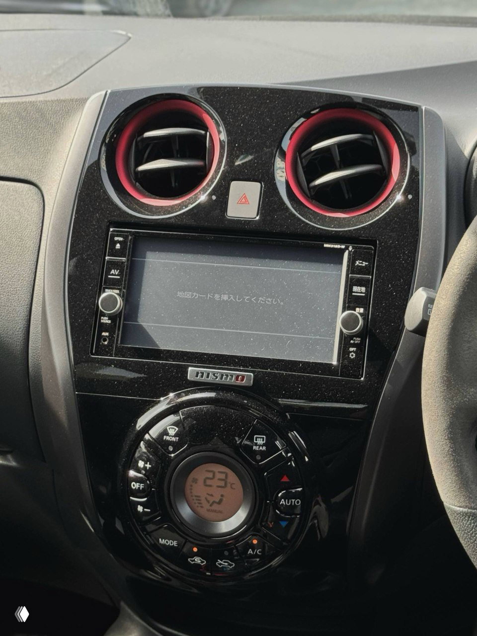 Центральная консоль Nissan Note Nismo ePower с мультимедиа-экраном, блоком климата и шильдиком NISMO, крупный план элементов управления и декоративных красных вставок.