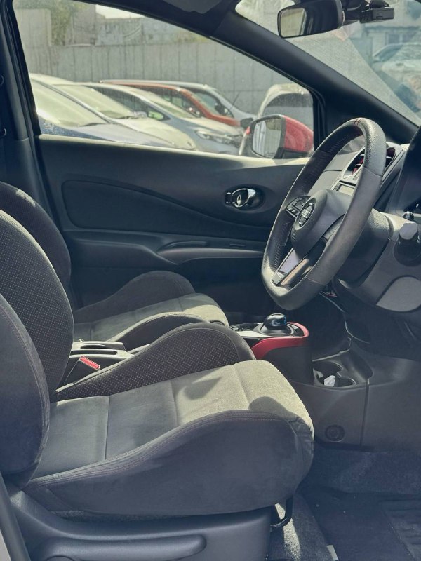 Вид салона Nissan Note Nismo ePower: передние сиденья, руль, торпедо и центральный тоннель, тканевая обивка сидений и спортивные элементы интерьера.