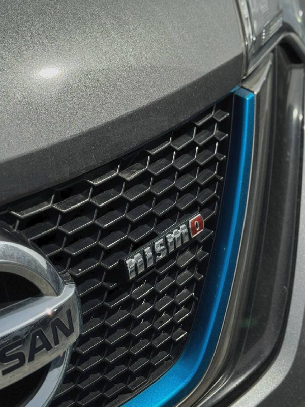 Крупный план передней решётки радиатора и эмблемы NISMO на Nissan Note Nismo ePower, декоративная синяя окантовка и логотип производителя на металлической решётке.