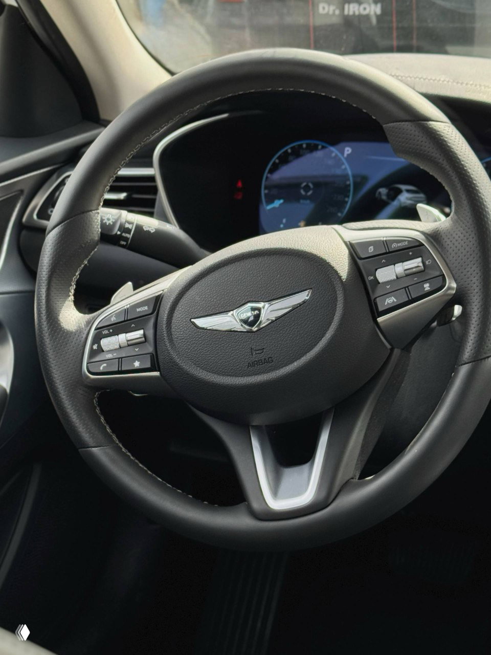 Кожаный руль Genesis с фирменной эмблемой и кнопками управления, вид на приборную панель из кабины, демонстрация состояния рулевого управления.