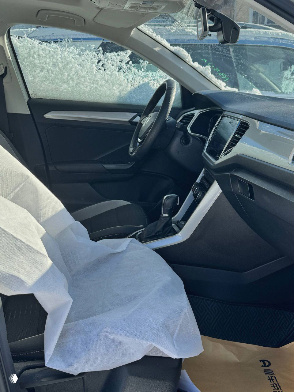 Передняя пассажирская часть салона Volkswagen T‑ROC с защитными чехлами на сиденьях — вид на дверь, сиденье и центральную консоль.