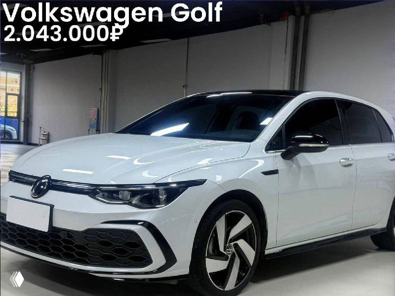 Фотография белого Volkswagen Golf 2022 года в выставочном зале; вид спереди-углом, заметны фирменный бампер, колёсные диски и логотип VW, указана цена.