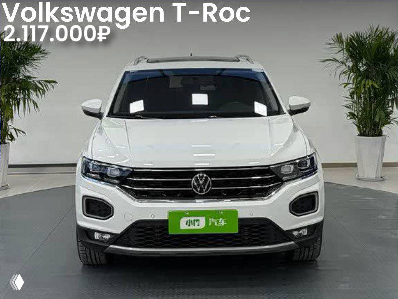 Фронтальный кадр белого Volkswagen T-Roc 2022 года в шоуруме Китая; видно решётку радиатора, передний бампер, зелёную табличку и указание цены и пробега.