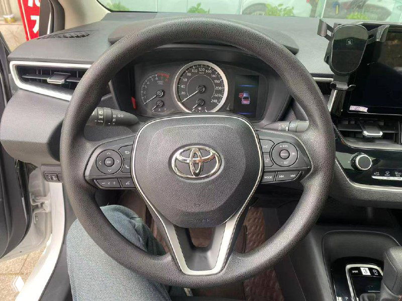 Крупный план руля Toyota Corolla 2023 с логотипом Toyota и панелью приборов; видна обивка торпеды и элементы управления на руле.