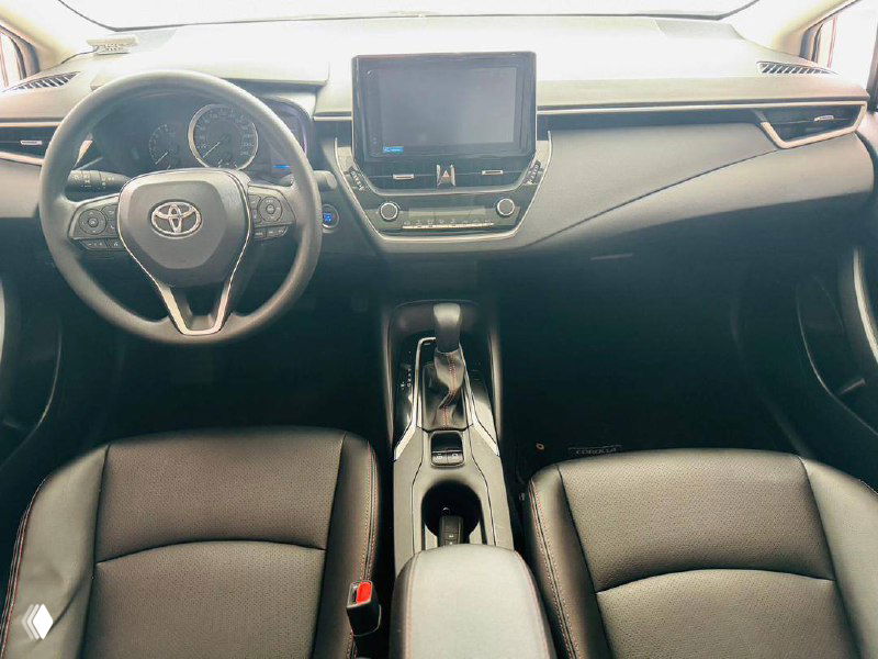 Интерьер Toyota Corolla 2022 — передняя панель, руль и передние сиденья в чёрной обивке, общий вид кабины водителя с центральной консолью.
