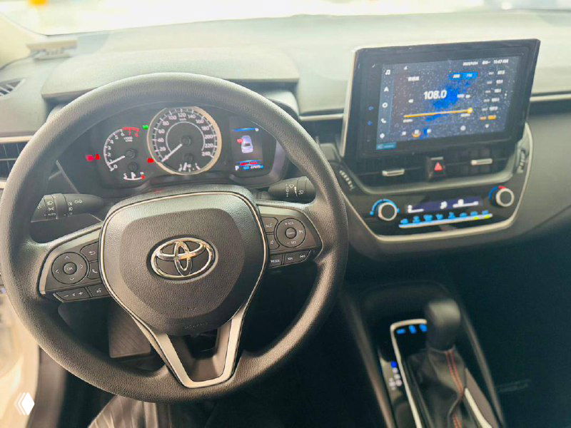 Панорамный вид салона Toyota Corolla 2022 с руля, приборной панели и центрального дисплея; вид подчёркивает состояние приборов и экран навигации.