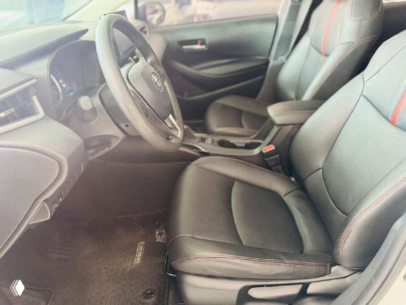 Сиденья водителя и пассажира Toyota Corolla 2022 — чёрная обивка с красной прострочкой, вид на кресла и подлокотник в хорошем состоянии.