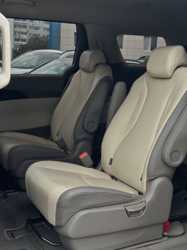 Ряд сидений второго ряда KIA Carnival в светлой тканевой обивке, вид на проход и подлокотники между сиденьями, просторный салон.