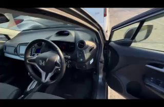 Салон и водительская зона Honda Insight 2011 с открытой дверью: рулевое колесо, торпедо, дверная обшивка и посадочное место водителя.