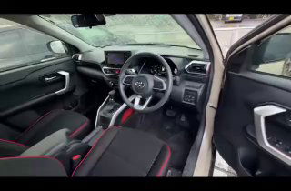 Распахнутая водительская дверь Toyota Raize 2021 с видом на руль, педали и пространство перед сиденьями — общий ракурс водительской стороны салона.