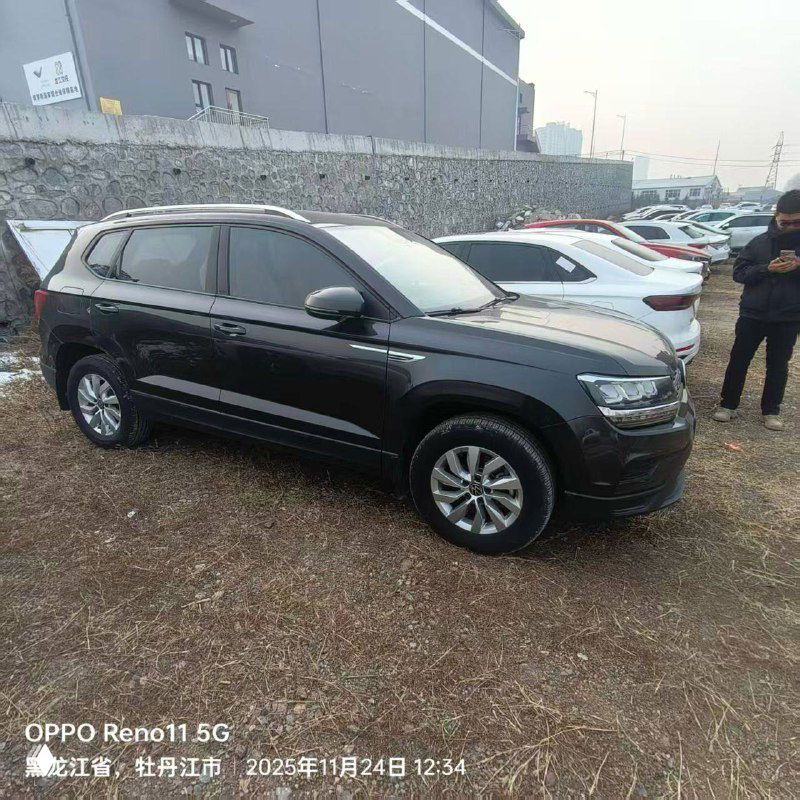 Тёмно-серый Volkswagen Tharu, боковой ракурс на стоянке в порту/складе в Китае, рядом другие автомобили и сотрудники на фоне.