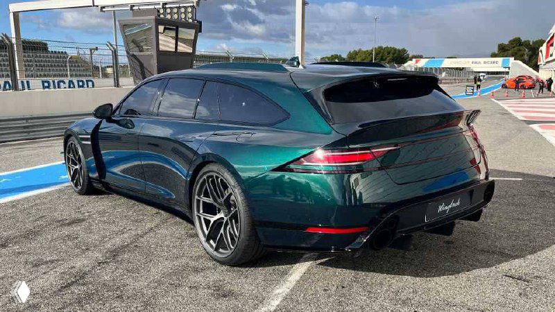 Задняя часть Genesis G90 Wingback на парковке пит-лейна, агрессивный задний диффузор и тонкие задние фонари на фоне боксов автодрома.