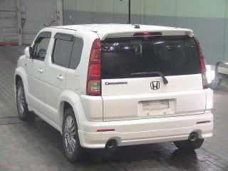 Белый Honda Crossroad 2008, вид сзади-угла в ангаре аукциона; видны задние фонари и бампер без номерного знака.