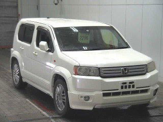 Белый Honda Crossroad 2008, крупный ракурс с переднего правого угла в ангаре аукциона; видны диски, пороги и передние фары.