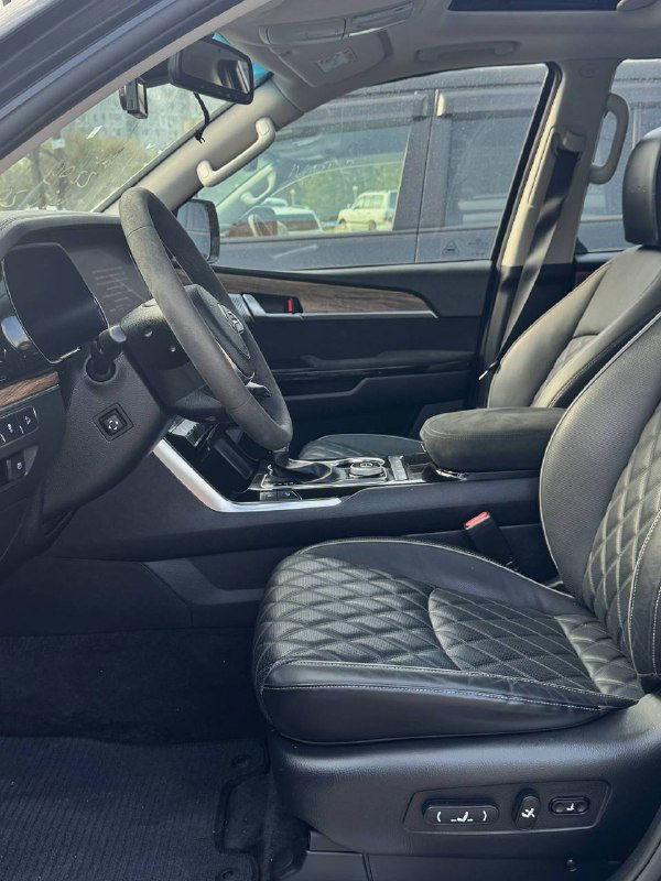 Передние кресла KIA Mohave с кожаной прошивкой, регулировки сидений и центральный подлокотник; интерьер в темных тонах.