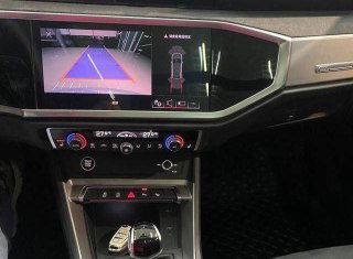 Экран медиасистемы Audi Q3 с изображением камеры и парковочных линий, блок климат-контроля и селектор коробки передач.