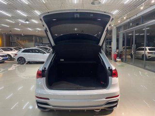 Открытый багажник Audi Q3: просторный отсек, ровный пол багажника и вид на заднюю часть автомобиля в шоуруме.