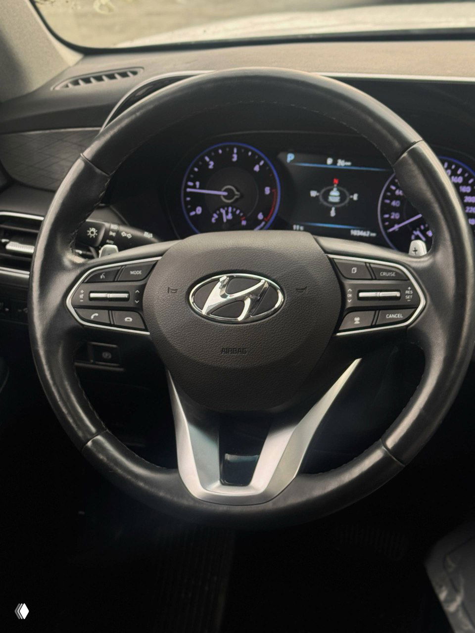 Крупный план рулевого колеса Hyundai с логотипом бренда, видна проектировка приборов и кнопки управления мультимедиа и круиз-контролем на спицах.