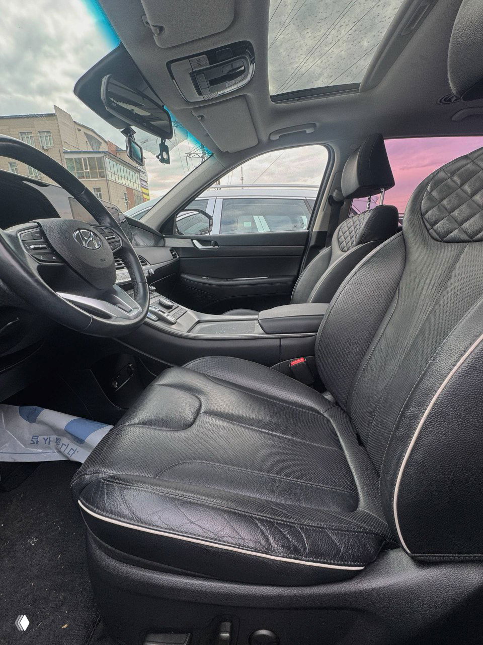 Композитный вид водительского места с кожаным сиденьем, подлокотником и видом через переднее боковое окно на припаркованные рядом машины; видна панорамная крыша.