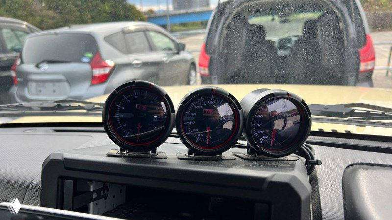 Три дополнительных круглых датчика давления и температуры на торпеде Suzuki Jimny Sierra 2021, крупный план приборов и интерьер в фоне.