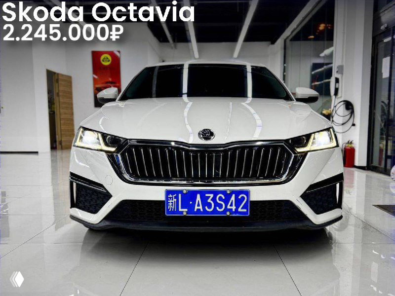 Фронтальная фотография белой Skoda Octavia в салоне; хорошо видна решётка радиатора, номер и указание цены 2.245.000₽.
