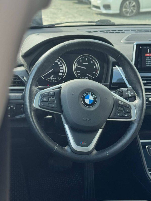 Крупный план рулевого колеса BMW внутри салона: видно логотип BMW на рулье, приборную панель и часть центральной консоли.