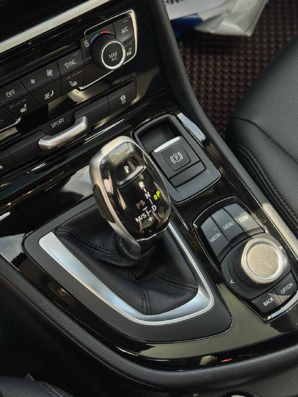 Крупный план селектора автоматической коробки передач BMW, видны окантовка, кнопки рядом и текстура отделки вокруг рычага.