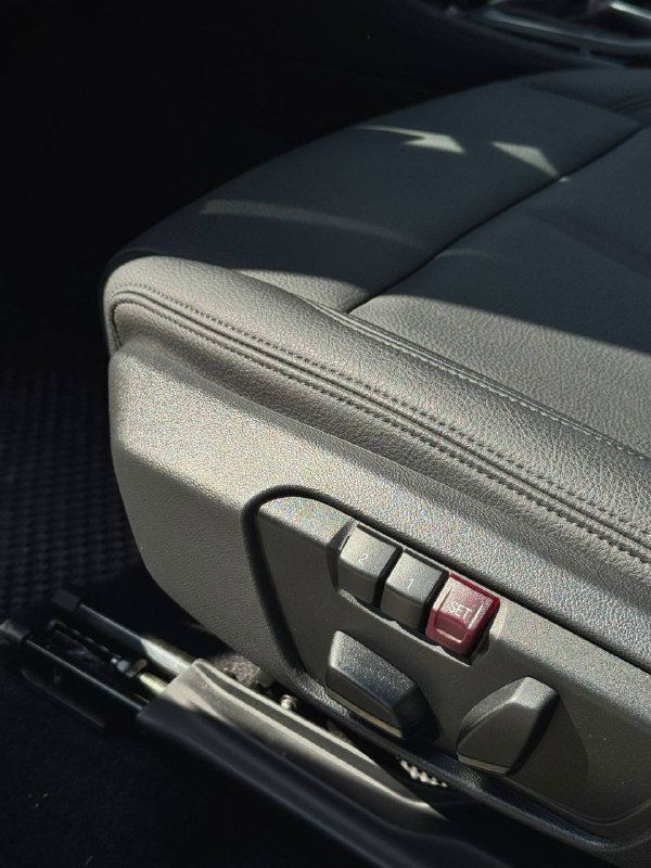 Боковая часть переднего кожаного сиденья BMW с элементами электропривода и регулировки положения сиденья, видна текстура обивки.