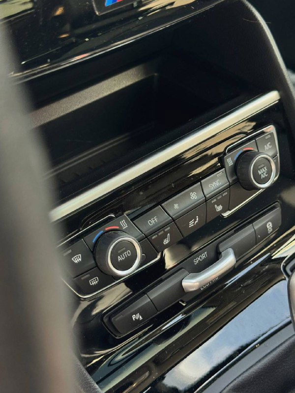 Панель климат-контроля BMW с кнопками и регуляторами, крупный план элементов управления температурой и вентиляцией в салоне.