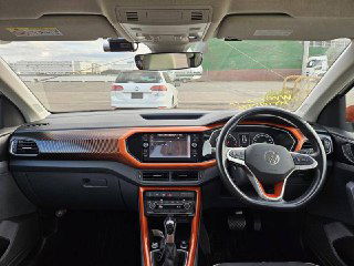 Широкий кадр салона Volkswagen T‑Cross 2021: приборная панель, мультимедиа экран и оранжевые акценты в оформлении торпедо и дефлекторов.