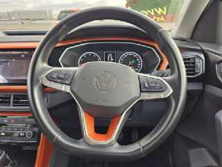 Крупный план рулевого колеса Volkswagen с логотипом VW и оранжевой декоративной окантовкой вокруг блока приборов и части торпедо, вид кнопок управления.