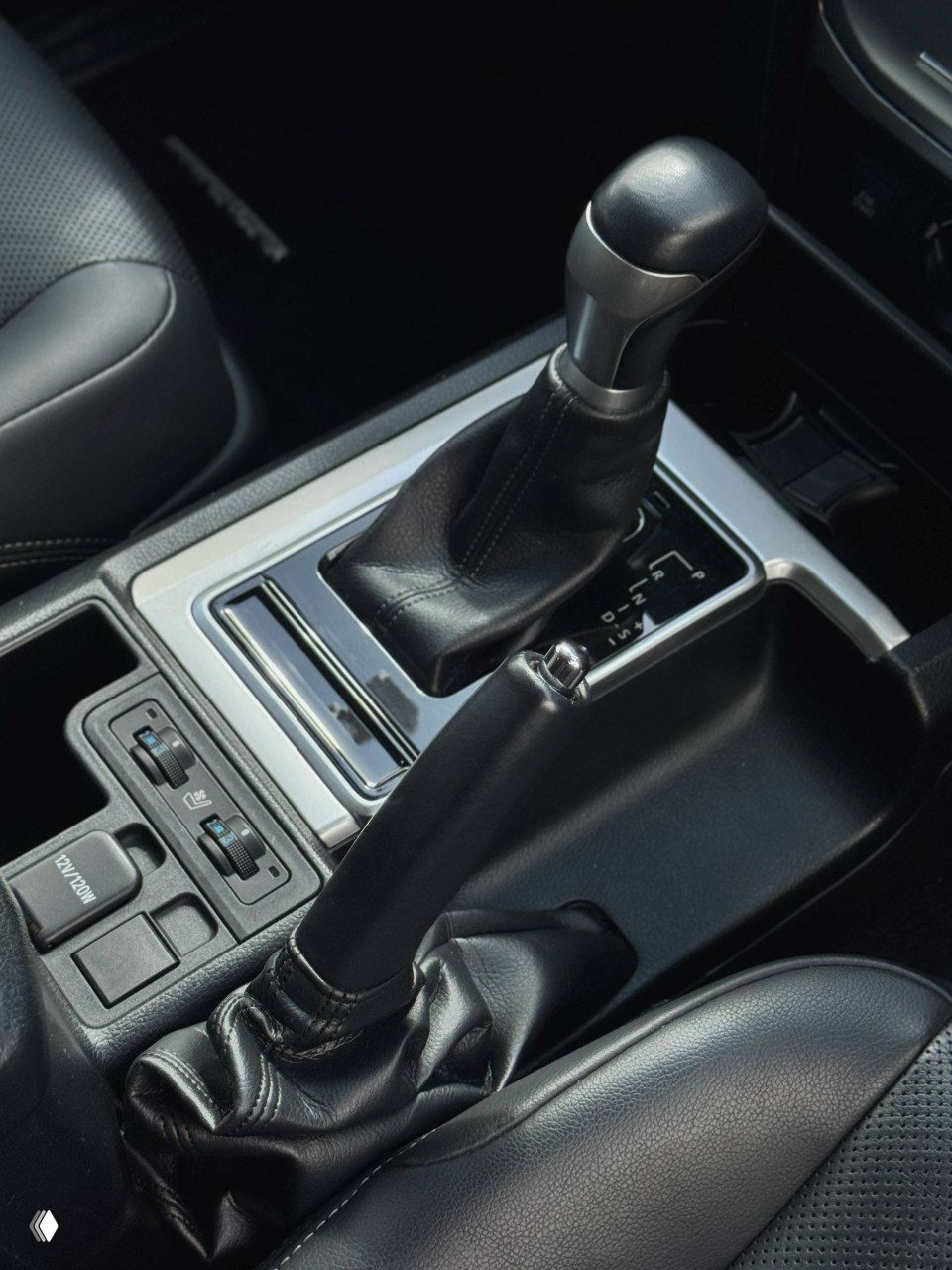 Рычаг переключения передач и ручной тормоз в центральной консоли Toyota Prado, вид на селектор, отделку и окружающие элементы управления.